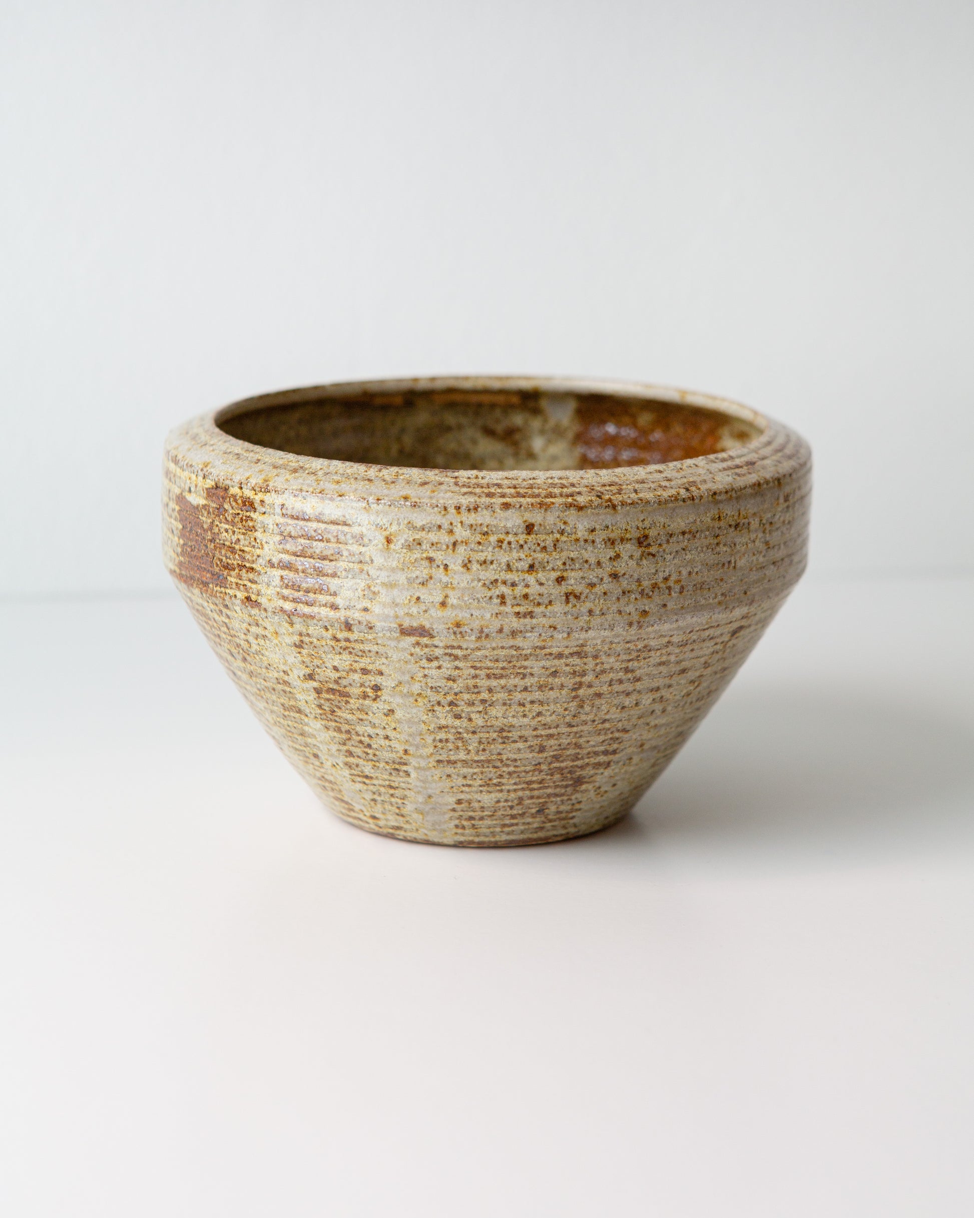 A handmade ceramic planter with a textured, ribbed exterior and a smooth, tapered interior, featuring a speckled glaze in earthy beige, brown, and cream tones, set against a plain light gray background.