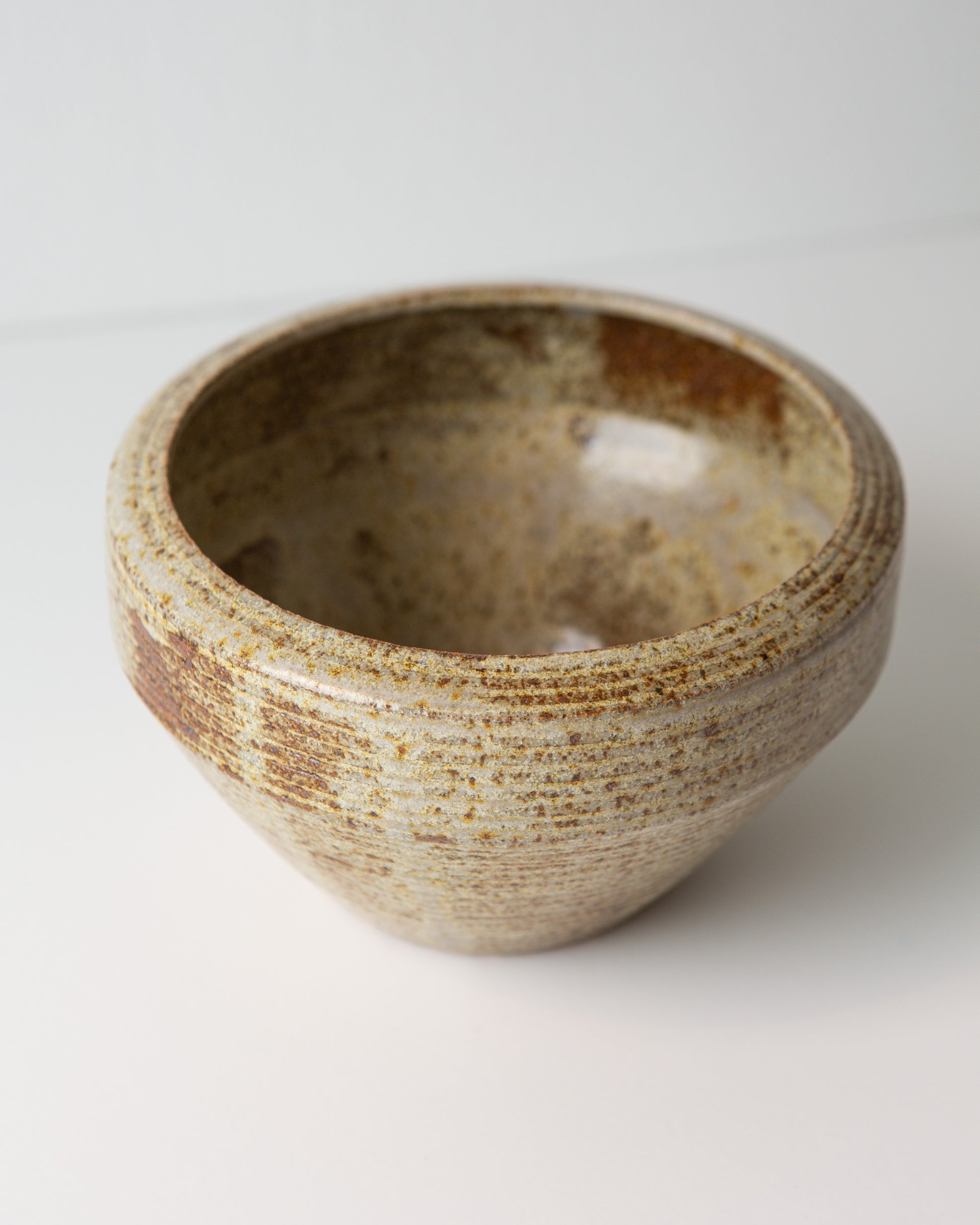 A handmade ceramic planter with a textured, speckled glaze in earthy beige, brown, and cream tones, photographed on a clean white background.