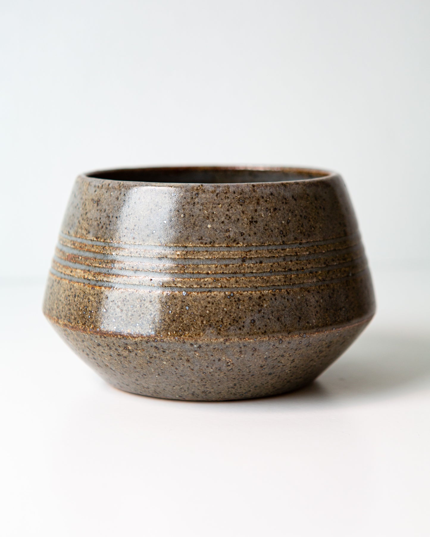 A small round ceramic bowl with a textured, speckled dark blue gray glaze, featuring horizontal ridges on the upper half, set against a plain white background.