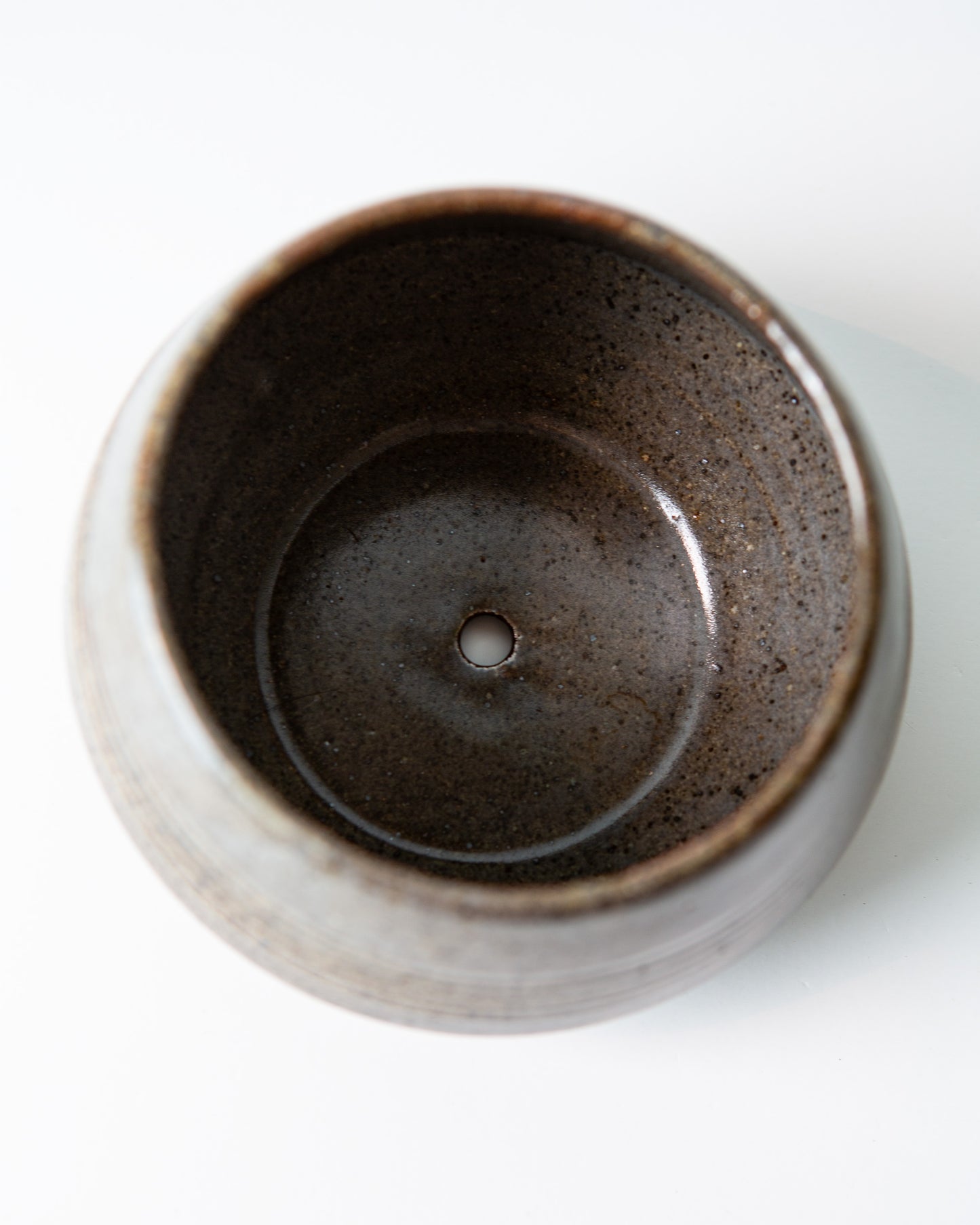 A top-down view of a round ceramic cup or small planter with a speckled dark blue grey interior, set against a plain white background.