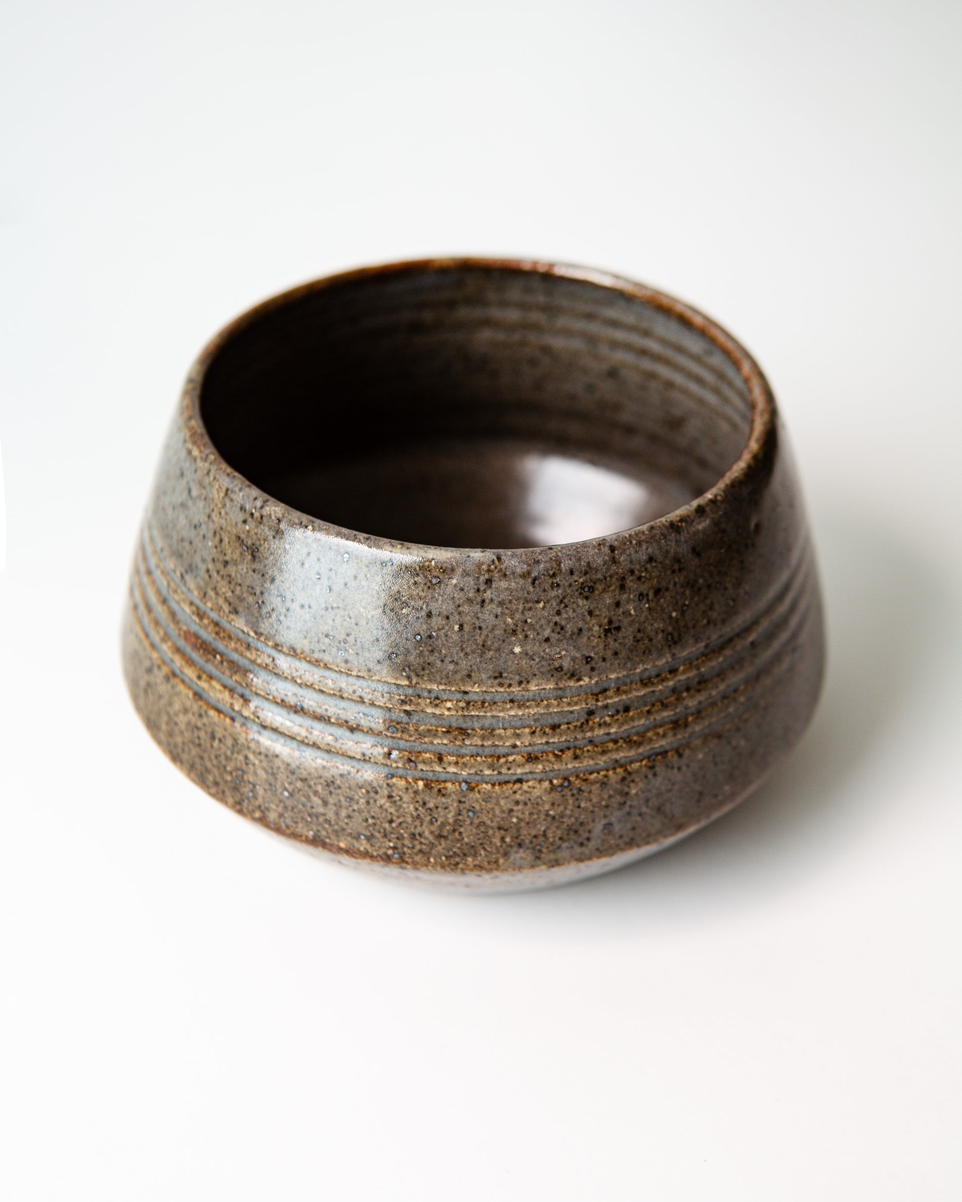 A circular planter with a blue/grey speckled glaze finish. There are 4 carved rings around the outside to add detail. The bottom angles inward. Shown on a plain white background.