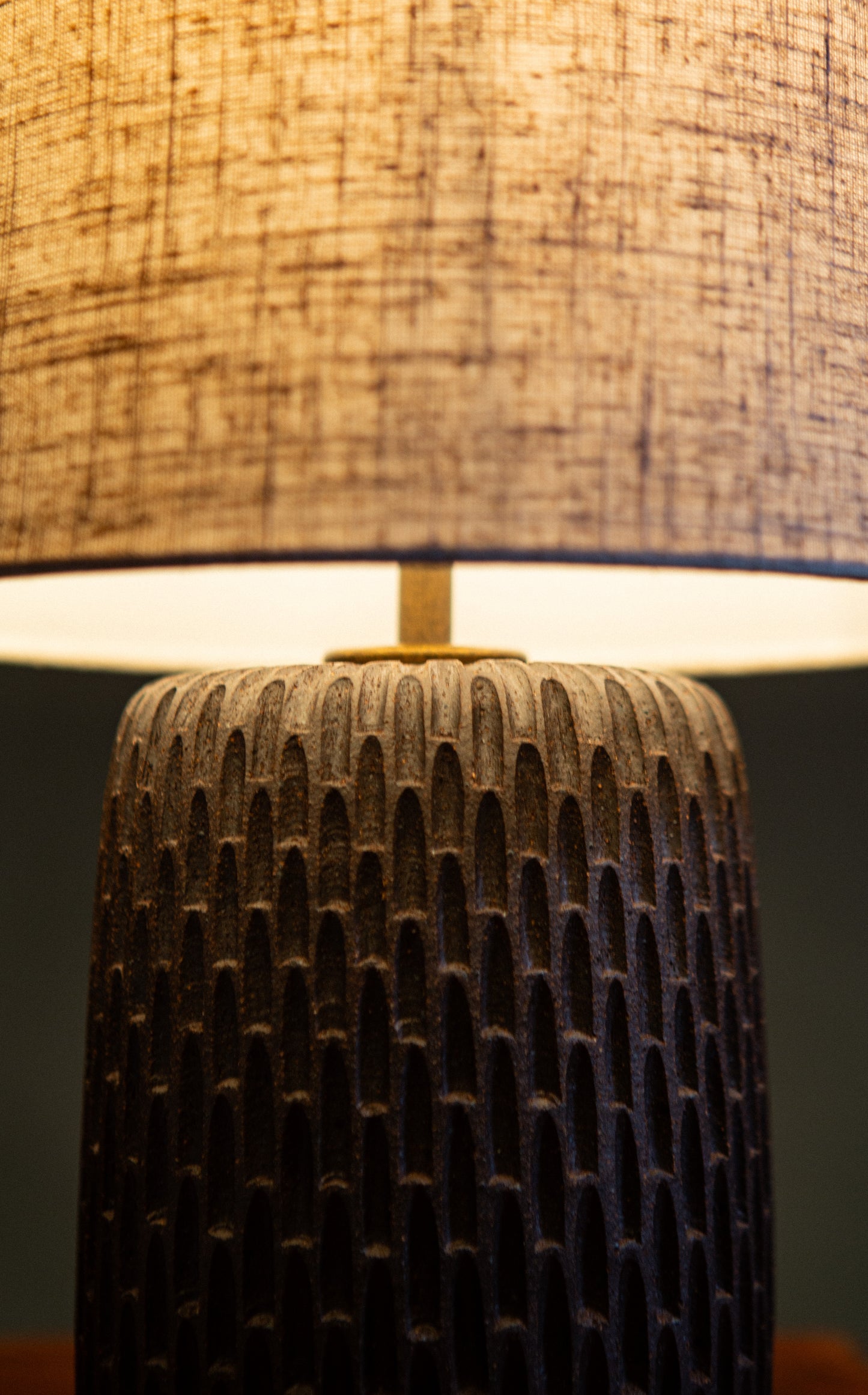 Close-up of a dark brown hand carved lamp with a dark base and light-colored shade.