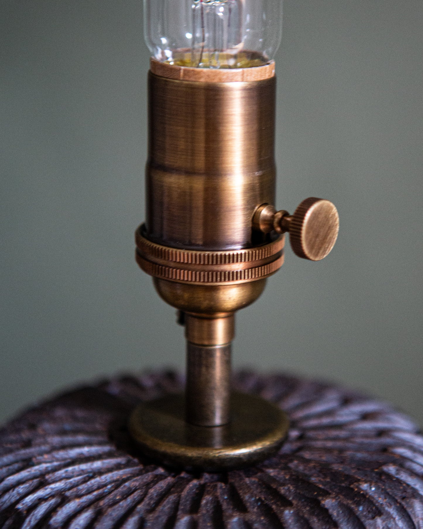 A close up showing the aged brass socket on the dark brown carved table lamp.