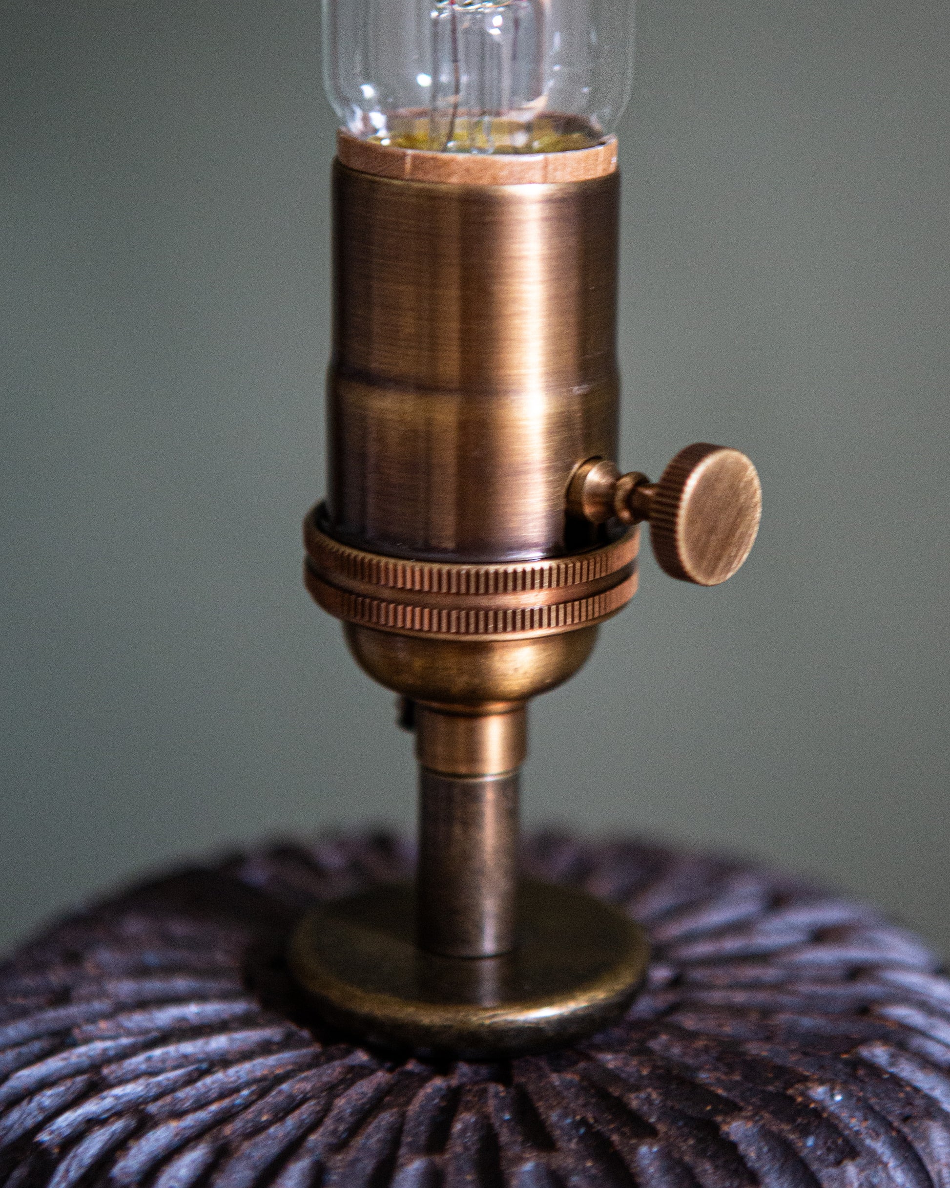A close up showing the aged brass socket on the dark brown carved table lamp.