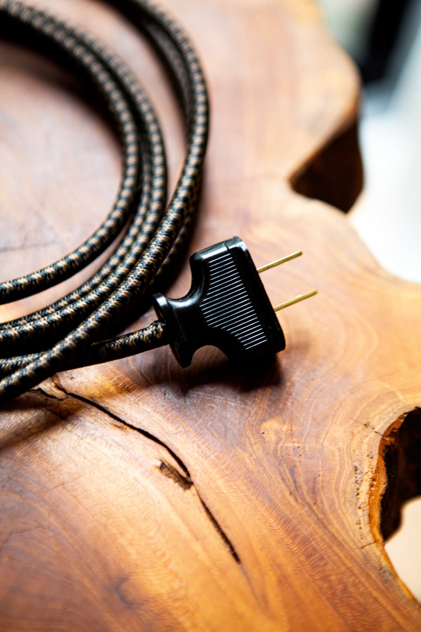 A dark brown chevron fabric chord attached to a black plug, sitting on a wood table.
