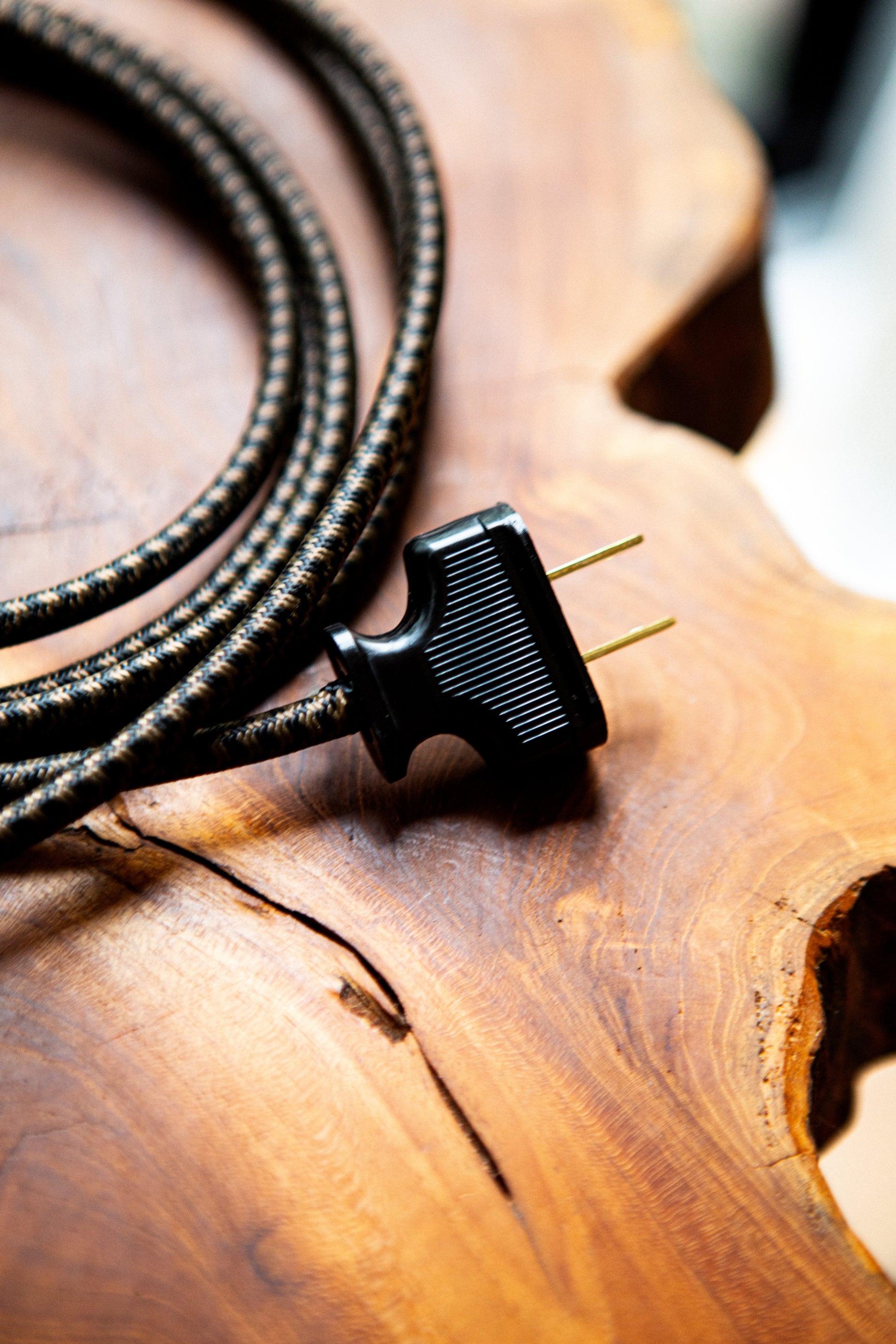 A dark brown chevron fabric chord attached to a black plug, sitting on a wood table.
