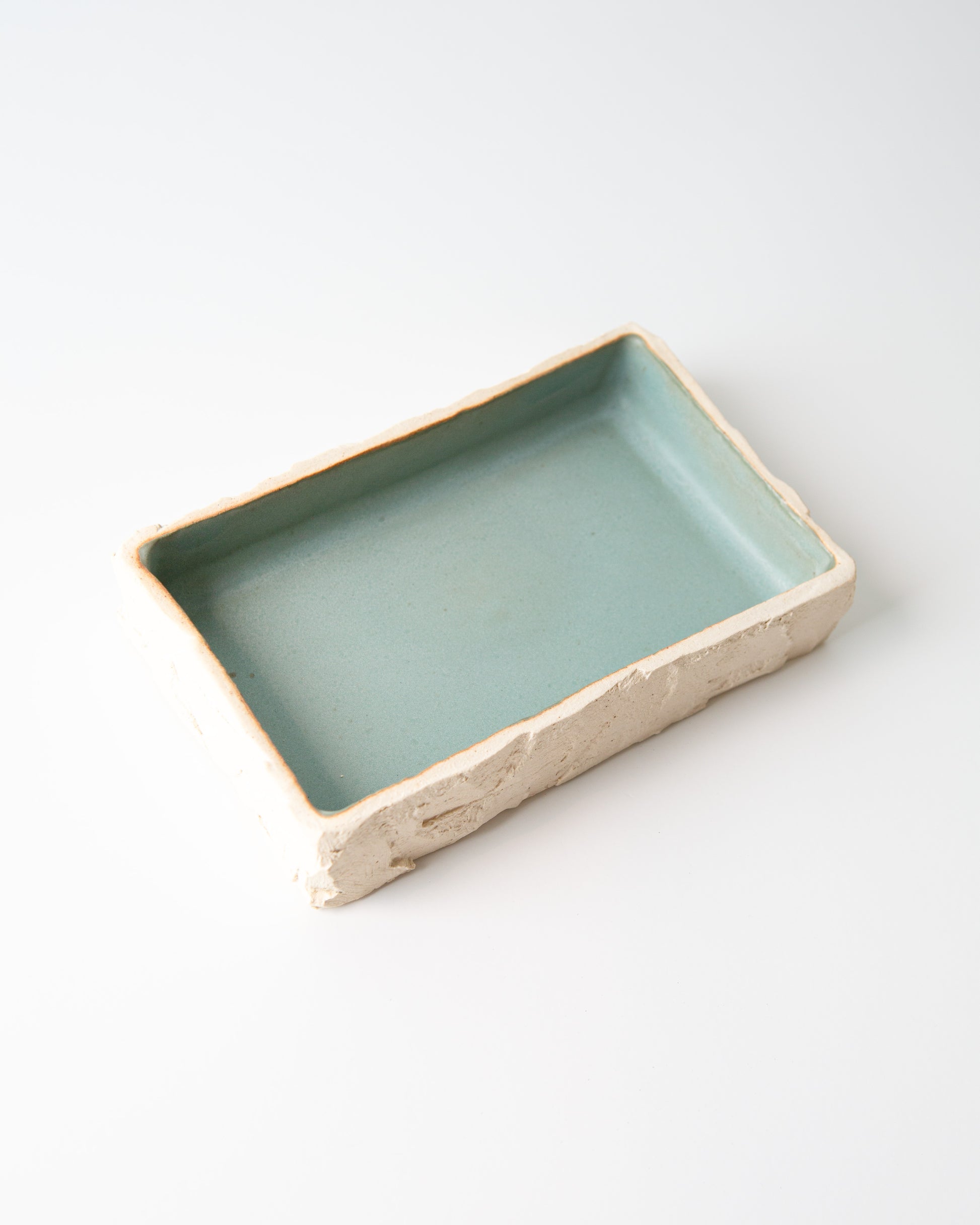 A rectangular ceramic dish with a hand-carved off-white clay exterior and a smooth, light teal glazed interior, shown on a clean white background.