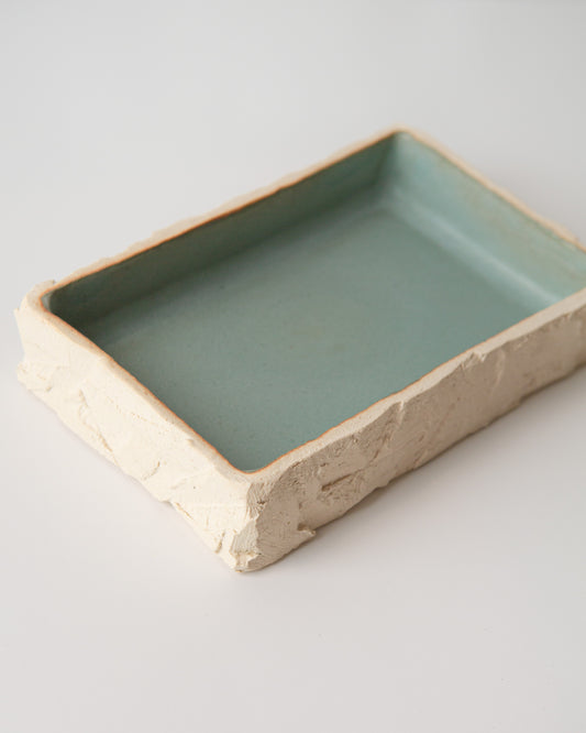 A closer view of the rectangular ceramic dish with a hand-carved off-white clay exterior and a smooth, light teal glazed interior, shown on a clean white background.